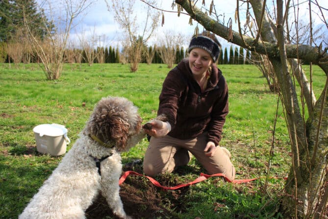 Alana McGee holds truffle with white truffle dog sitting next to her